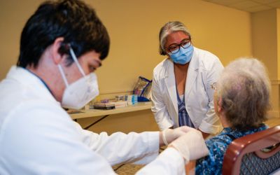 Cherokee Layson-Wolf, PharmD, BCACP, FAPhA, professor of practice, sciences, and health outcomes research, speaks with a patient as a UMSOP student gives a vaccine.