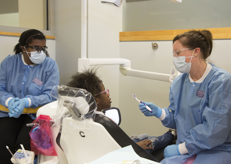 University of Maryland School of Dentistry students Jennine Jarrett, left, and Shannon Burke discuss oral health while caring for CURE Scholar Mariah Beatty, a sixth-grader at Green Street Academy.