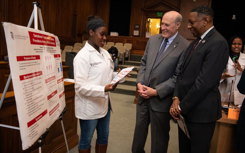Shereen Farquharson (left), a CURE Scholar in cohort 2, presents her research poster to UMB Interim President Bruce E. Jarrell, MD, FACS (center), and Del. Keith Haynes at the Legislative Services Building in Annapolis.