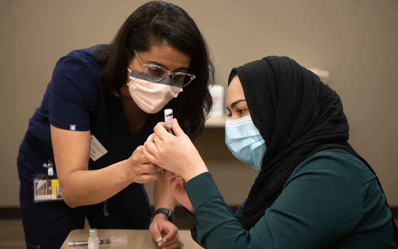 Amna Kahn, a first-year student at the University of Maryland School of Pharmacy (right), learns how to prep the COVID-19 vaccine doses.