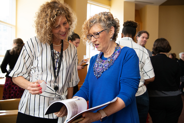 The School of Medicine’s Marianne Cloeren (right) shows a colleague the necklace she’s wearing that is in the “1807” journal.