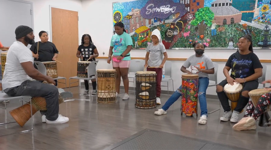 Participants in the Moving History Summer Enrichment Program at the Community Engagement Center learn about African history and culture with a drum circle.