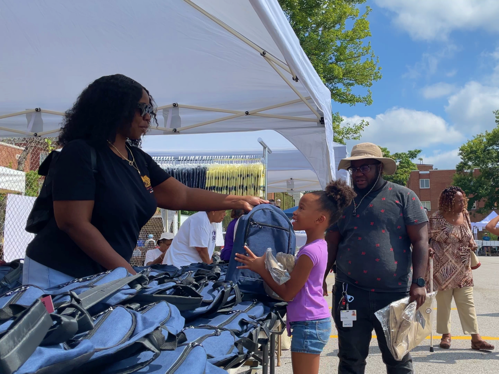 Young girl receiving a free blue backpack from an adult at the Back to School Bash