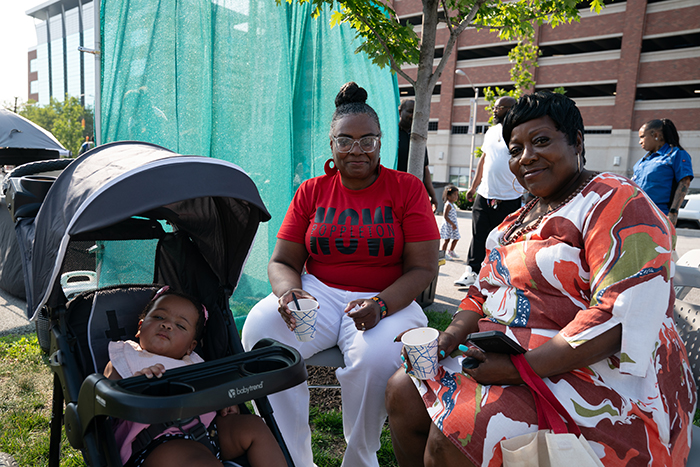 Two attendees take a quiet break in the shade as a young child naps peacefully in a stroller during the Juneteenth Jubilee.