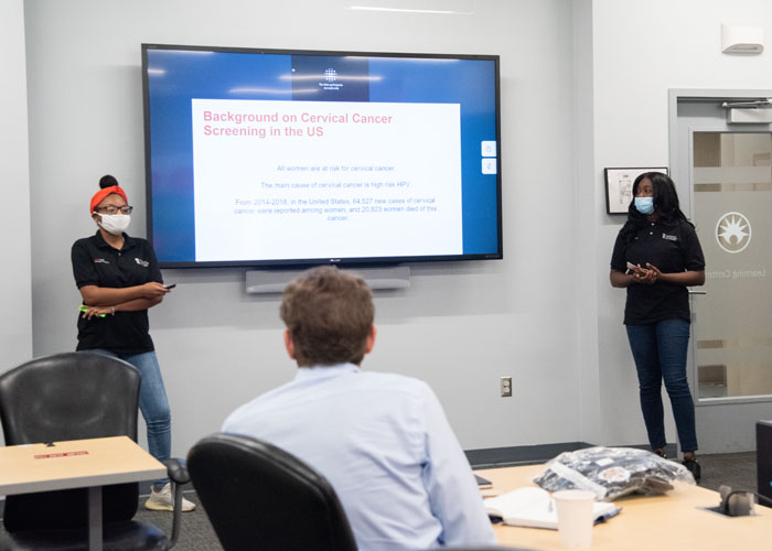 Markia Eubanks (left) and Ayishat Yussuf (right), both students in Cohort 1 of the UMB CURE Scholars Program, present their research on HPV and cervical cancer at Becton Dickinson. 