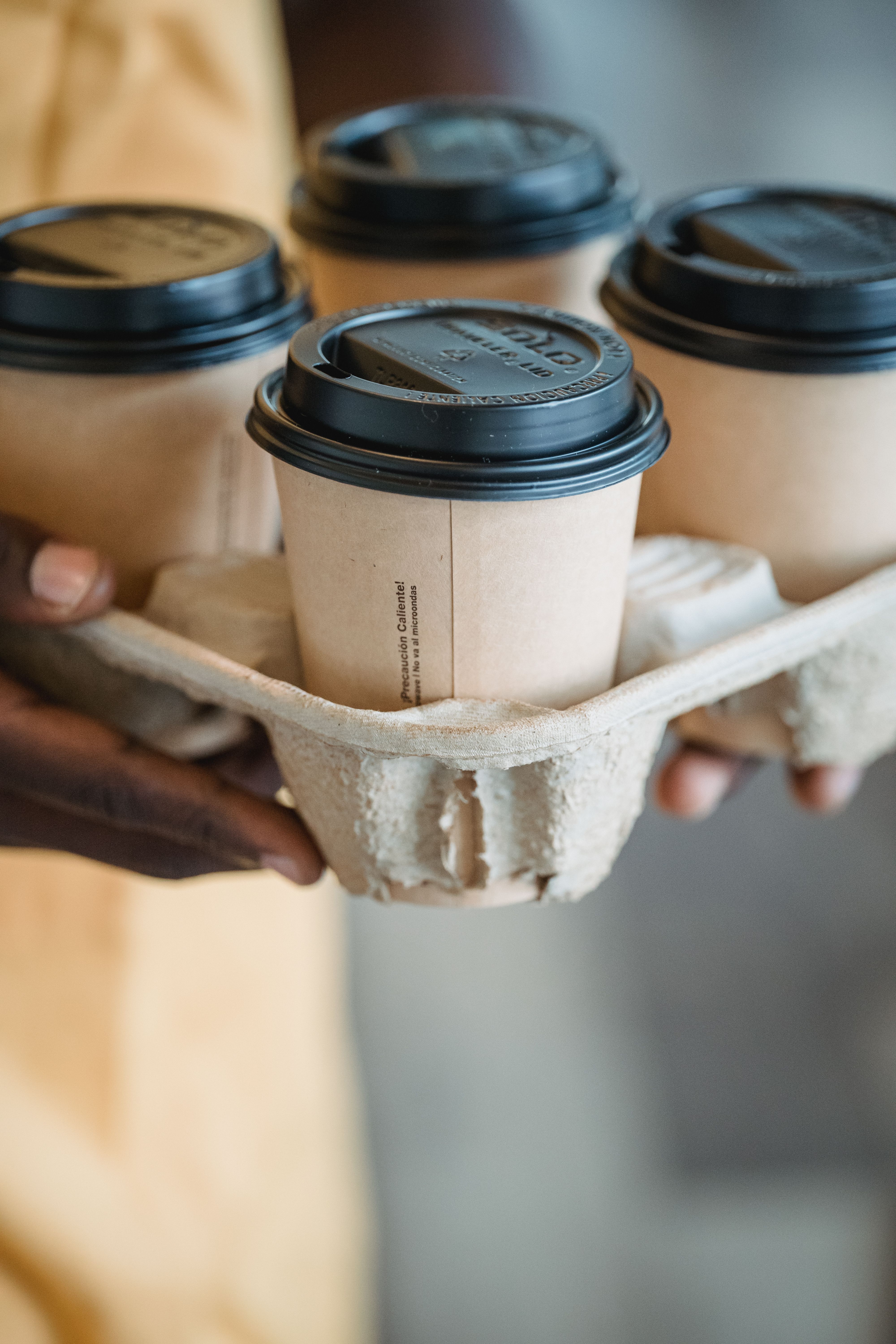 A close up of hands holding a tray of coffee cups.