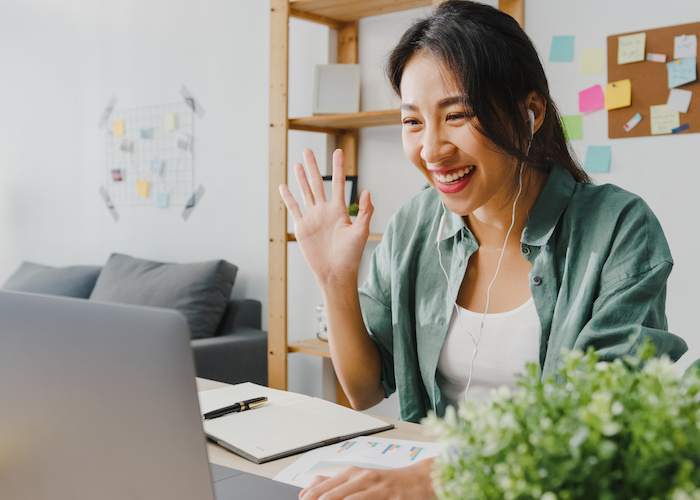 person smiling and waving at computer during video meeting