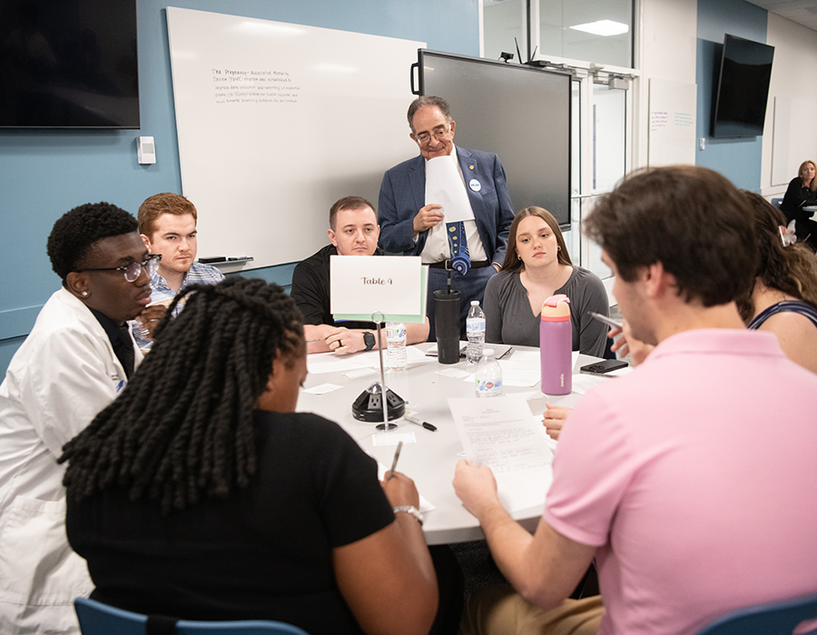 Group of UMB students discussing topics watched over by Chancellor Jay Perman.