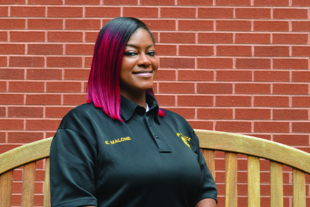 Portrait of Officer Erika Malone in front of bricks while sitting on a light brown bench