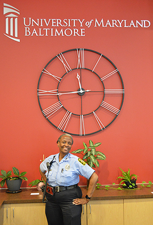Portrait of officer Evelyn Greenhill in front of a red wall and an industrial clock