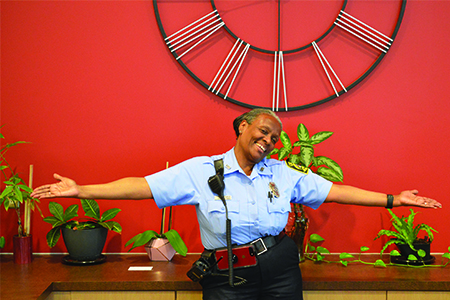 Portrait of officer Evelyn Greenhill in front of a red wall and an industrial clock