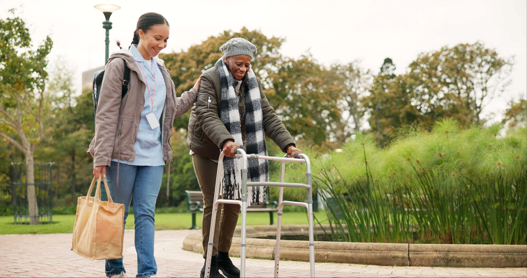 A woman helping an older woman walk while she is using a walker