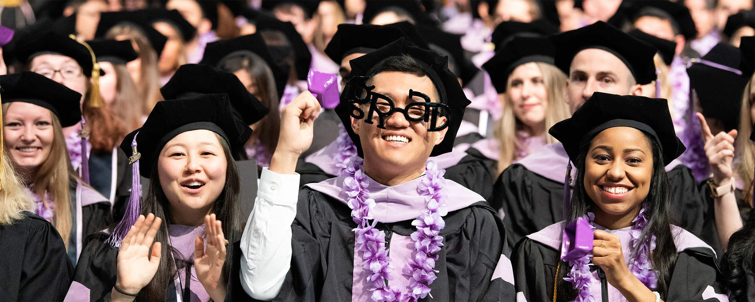students in commencement regalia celebrate, one wears 